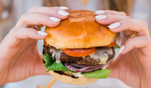 A girl holding a meat burger with tomato, onion and salad