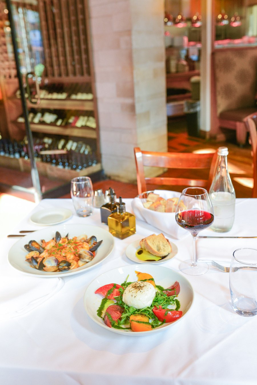 A table with spaghetti with frutti di mare a salad with tomato and mozzarella, a glass of wine and a glass of water